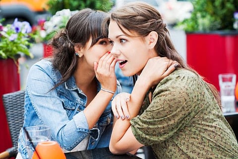 Two female friends sitting in a sidewalk cafe, whispering away some secret 