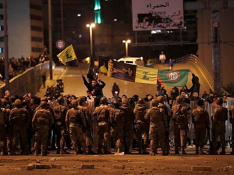 Supporters of the Iran-backed militant group hold the flags of Shiite Hezbollah and Amal Movement groups, as they stand in front of Lebanese army soldiers after a clash erupted between the anti-government protesters and them, in Beirut