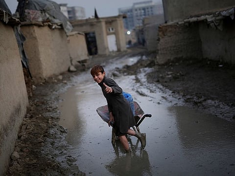 An Afghan boy gives a thumbs up as he pushes a wheelbarrow through a muddy lane at a camp in Kabul, Afghanistan, Wednesday, Nov. 27, 2019. 