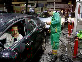 A worker fills up a car's tank at a petrol station.