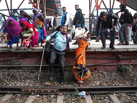 44-year-old blind man Vinod Kumar Sharma (L) walks from a platform onto the rail tracks with his wife Indrapti (R) after arriving at Okhla railway station in New Delhi.