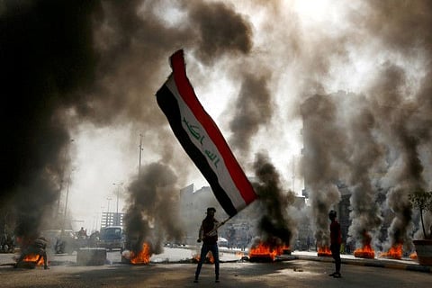 A protester holds an Iraqi flag amid a cloud of smoke from burning tires during ongoing anti-government protests in Najaf, Iraq 