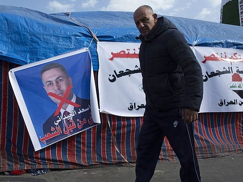 A protester walks past a poster with defaced picture of Iraqi politician Assad al-Edani, and Arabic that reads his name and “rejected by the people,” during the ongoing protests, in Tahrir square, in Baghdad, Iraq, Wednesday, Dec. 25, 2019. 