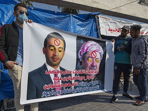 Protesters carry a poster with defaced pictures of Iraqi Parliament Speaker Mohammed al-Halbousi, left and Chairman of the Kurdish Democratic Party and former president of the Iraqi Kurdistan Region Masoud Barzani, with Arabic that reads, "we want an equitable election law, you are both included," in Tahrir Square, Baghdad, Iraq, Monday, Dec. 23, 2019. 