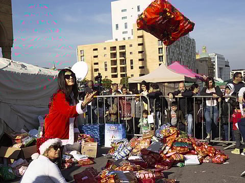 In this Sunday, Dec. 22, 2019, photo, volunteer Ibtisam Nablussi tosses a Christmas present as anti-government protesters distribute clothing to the needy ahead of Christmas at Martyrs Square in Beirut, Lebanon. 
