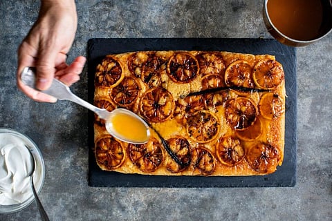 Lemon-maple butter is drizzled onto Yotam Ottolenghi’s upside-down lemon sponge cake, still warm from the oven, in New York, Dec. 8, 2019. Wrapping a cake with parchment paper and foil before it gets its long, slow bake ensures not only the “ta-da!” element once it’s revealed, but also the retention of flavor and moisture within the cake when it’s served. (Andrew Scrivani/The New York Times)