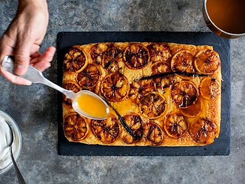 Lemon-maple butter is drizzled onto Yotam Ottolenghi’s upside-down lemon sponge cake, still warm from the oven, in New York, Dec. 8, 2019. Wrapping a cake with parchment paper and foil before it gets its long, slow bake ensures not only the “ta-da!” element once it’s revealed, but also the retention of flavor and moisture within the cake when it’s served. (Andrew Scrivani/The New York Times)