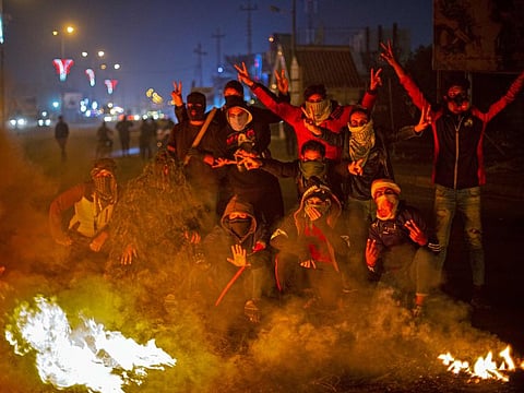 Iraqi anti-government protesters gather by a fire at a make-shift roadblock in the southern city of Basra on December 24, 2019.