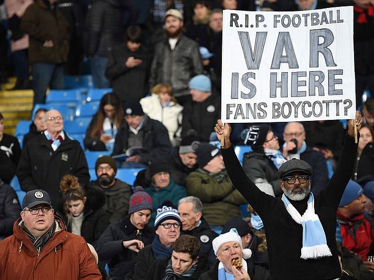 A Manchester City fan holds up a banner complaining about VAR. 
