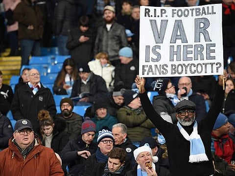 A Manchester City fan holds up a banner complaining about VAR. 