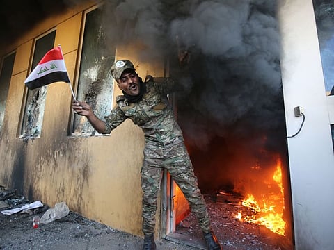 A member of Iraq's Hashed al-Shaabi military network waves a national flag as he exits a burning room after breaching the outer wall of the US diplomatic mission in the capital Baghdad, on December 31, 2019, during a rally to vent anger over weekend air strikes that killed pro-Iran fighters in western Iraq. 