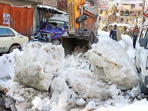 Residents watch as an excavator removes snow boulders on a road, after a heavy snowfall in the Neelum Valley, near the Line of Control (LoC), on Tuesday.