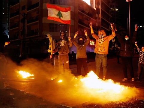 Anti-government demonstrators hold a national flag as burning tires block a road during a protest in Beirut, Lebanon, Thursday, Jan. 16, 2020.