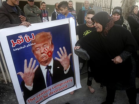 A Palestinian woman beats by her shoes a banner that shows a portrait of the U.S. President Donald Trump with Arabic words that read:"Your suspicious deal will not pass," during a protest against the White House plan for ending the Israeli-Palestinian conflict, at Rashidiyeh Palestinian refugee camp, southern Lebanon, Wednesday, Jan. 29, 2020. 