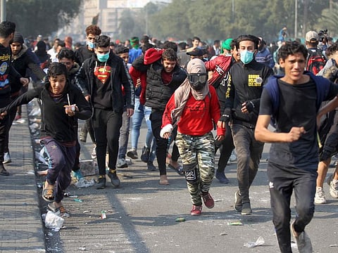 Iraqi protesters rush for cover amid clashes with riot police following a demonstration  in Al Wathba Square in Baghdad on January 30.