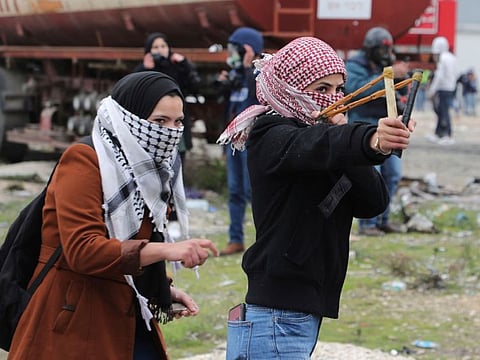 A Palestinian demonstrator uses a sling shot to hurl rocks at Israeli occupation forces during clashes following rally protesting a US peace plan proposal, at the northern entrance of the West Bank city of Ramallah near the Jewish colony of Beit El, on February 1, 2020. 