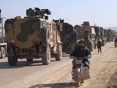 In this frame grab from video taken on Sunday, Feb. 2, 2020, people ride their motorcycles next to a Turkey Armed Forces convoy is seen at the northern town of Sarmada, in Idlib province, Syria. 