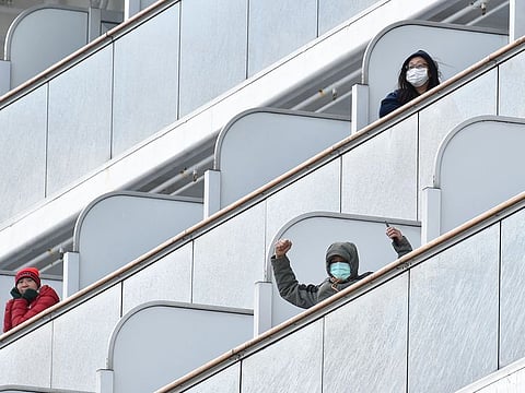 A passenger aboard the Diamond Princess cruise ship waves to the media upon arriving at Yokohama port on February 6, 2020. Ten more people on a cruise ship off Japan have tested positive for the new coronavirus, local media said, raising the number of infections detected on the boat to 20. 