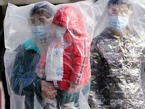 Passengers wearing masks and covered with plastic bags walk outside the Shanghai railway station in Shanghai