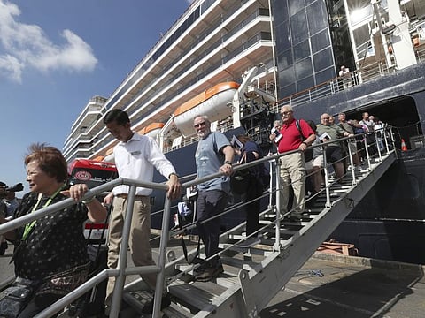 Passengers of the MS Westerdam, back, owned by Holland America Line, disembark at the port of Sihanoukville, Cambodia, Saturday, Feb. 15, 2020. After being stranded at sea for two weeks because five ports refused to allow their cruise ship to dock, the passengers of the MS Westerdam were anything but sure their ordeal was finally over. (AP Photo/Heng Sinith)