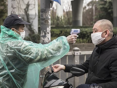A security guard takes the temperature of a man wearing a protective mask at an entrance to a fresh produce market in Shanghai, China, on Saturday, Feb. 15, 2020. China is entering the "most critical time" in its fight to contain the spreading coronavirus, a government official said. Photographer: Qilai Shen/Bloomberg