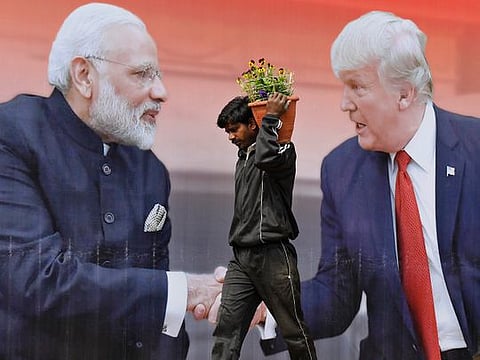 An Indian worker walks carrying flowers to plant passes a billboard featuring Donald Trump and Narendra Modi, in Agra, India