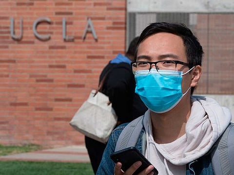 A student wears a face mask to protect against the COVID-19 (Coronavirus) as he leaves the campus of the UCLA college in Westwood, California 