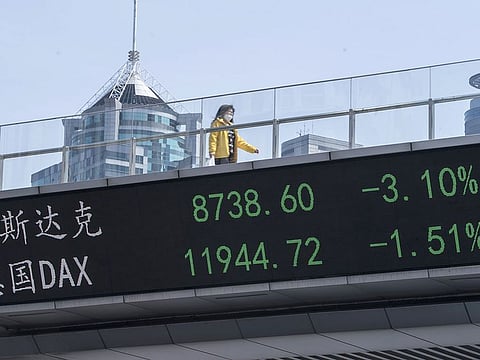A pedestrian wearing a protective mask walks along an elevated walkway as an electronic ticker displays stock figures in Pudong's Lujiazui Financial District in Shanghai, China, on Friday, March 6, 2020. While infections in the rest of the world accelerate, the coronavirus epidemic is showing signs of easing at its center -- China -- with new cases slowing dramatically and recoveries gathering pace. 