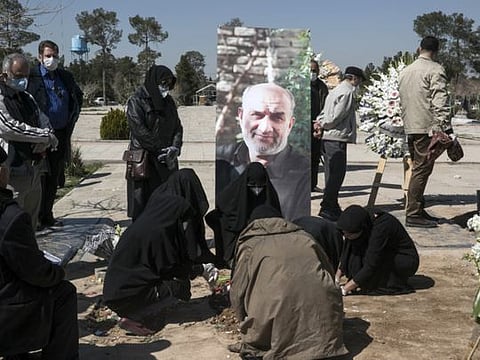 Relatives wearing face masks mourn over the grave of former politburo official in the Revolutionary Guard Farzad Tazari, shown in poster, who died Monday after being infected with the new coronavirus, at the Behesht-e-Zahra cemetery just outside Tehran on Tuesday.