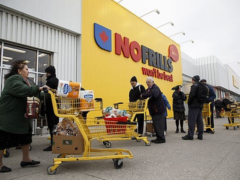 A shopper pushes a cart filled with paper towels and supplies as others wait in line to enter a No Frills supermarket in Toronto, Ontario, Canada on Saturday, March 14, 2020. 