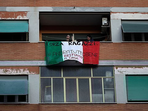 People stand on a balcony adorned with an Italian flag during one of the many flash mobs taking place these days in Rome, Sunday, March 15, 2020. The nationwide lockdown to slow coronavirus is still early days for much of Italy, but Italians are already showing signs of solidarity with flash mob calls circulating on social media for people to ''gather'' on their balconies at certain hours, either to play music or to give each other a round of applause. For most people, the new coronavirus causes only mild or moderate symptoms. For some, it can cause more severe illness, especially in older adults and people with existing health problems.