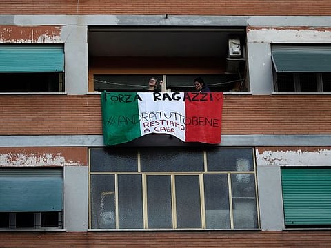 People stand on a balcony adorned with an Italian flag during one of the many flash mobs taking place these days in Rome, Sunday, March 15, 2020. The nationwide lockdown to slow coronavirus is still early days for much of Italy, but Italians are already showing signs of solidarity with flash mob calls circulating on social media for people to ''gather'' on their balconies at certain hours, either to play music or to give each other a round of applause. For most people, the new coronavirus causes only mild or moderate symptoms. For some, it can cause more severe illness, especially in older adults and people with existing health problems.