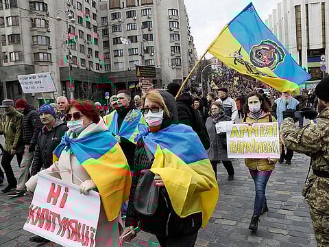 Participants wearing protective masks as a preventive measure against the coronavirus (COVID-19) attend a rally on the Volunteer Day honouring fighters, who joined the Ukrainian armed forces during a military conflict in the country's eastern regions, in Kiev, Ukraine March 14, 2020. The placard reads "No to capitulation". 