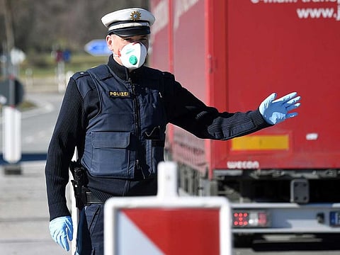 A German police officer, wearing a face mask, stops a driver at the border crossing between Austria and Germany, near the German village of Oberaudorf, as Germany imposes border controls with five countries in a virus fightback, on March 16, 2020. 