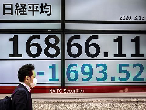 A man wearing a protective face mask, following an outbreak of the coronavirus (COVID-19), walks past a screen showing the Nikkei index outside a brokerage in Tokyo.  Asian stock markets and U.S. futures fell Monday after the Federal Reserve slashed its key interest rate to shore up economic growth.