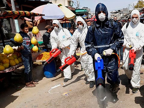 Workers wearing protective gear spray disinfectant as a precaution against the coronavirus, at the main market in Gaza City on March 19, 2020.