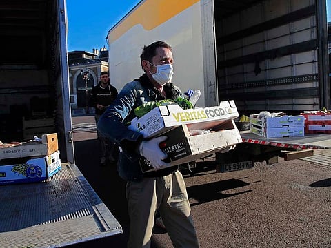 A worker wearing a face mask transfer food from one to an other truck in Versailles, west of Paris, Tuesday, March 24, 2020.