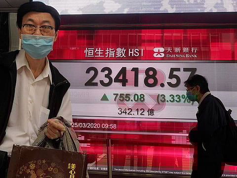 A man wearing a face mask walks past a bank's electronic board showing the Hong Kong share index at Hong Kong Stock Exchange Wednesday, March 25, 2020. Shares have advanced in Asia after the Dow Jones Industrial Average surged to its best day since 1933 as Congress and the White House neared a deal.