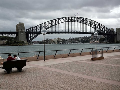 People sit on a bench at the mostly deserted promenade of the Sydney Opera House overlooking the Sydney Harbour Bridge, in the wake of New South Wales implementing measures to prevent the spread of COVID-19 (File) 