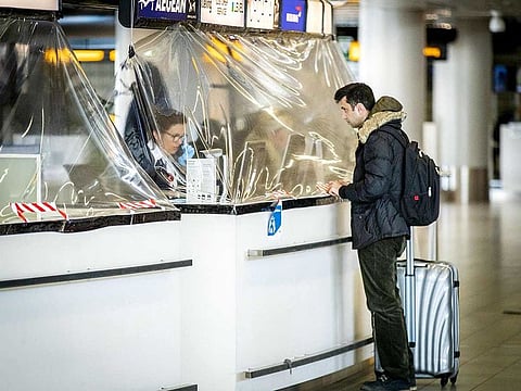 A passenger stands at an airline counter protected with a plastic tarpaulin on March 27, 2020 at the Amsterdam Schiphol airport which operates on lower level due measures to curb the spread of the COVID-19 and a lower number of travellers.