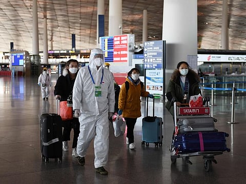 An airport worker escorts passengers through the empty departure area in Beijing Capital Airport on March 27, 2020.  China will drastically cut its international flight routes and bar entry to returning foreigners based in the country to stem the spread of the COVID-19 coronavirus, authorities said on March 26.