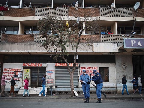 A South African police officer clears a jammed pump rifle of a colleague while enforcing social distancing making shoppers stretch their arms in front of them to ensure that they are at least one metre apart from one another while they queue outside a supermarket in Hillbrow, Johannesburg, on March 28, 2020.