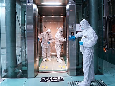 Members of a medical team wearing protective suits spray disinfectants on an elevator, in Dubai. 