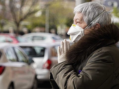 A member of the public, wearing a protective face mask and gloves, offers a prayer outside the Palacio de Hielo ice rink, temporarily converted into a morgue for victims of COVID-19, in Madrid, Spain, on Monday, March 30, 2020. 