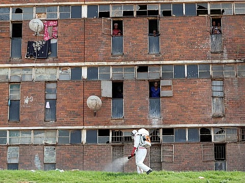Residents look out of the window as a worker wearing protective gear sprays disinfectant to sanitise parts of the Alexandra's Madala Men's Hostel during a 21-day nationwide lockdown to try to contain the coronavirus disease (COVID-19) outbreak, in Alexandra, South Africa April 1, 2020.