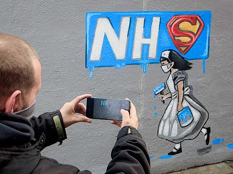 A man takes a photograph of a mural in honour of the NHS amid the growing coronavirus outbreak, in Pontefract, England, Friday April 3, 2020.