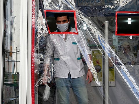 A pharmacist wears a mask next to a door covered in plastic to avoid contamination in Casablanca, Morocco, Friday March 27, 2020.