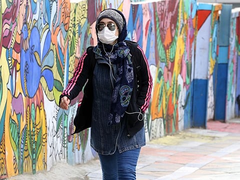 A Iranian woman wearing a protective mask walks past graffiti on a wall in Tehran on April 13 during the COVID-19 pandemic. 