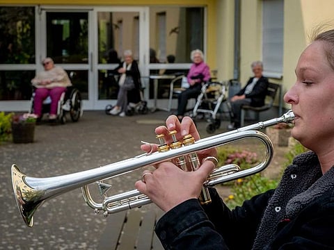 A young musician plays the trumpet in the garden of a retirement and nursing home in Karben near Frankfurt, Germany, Monday, April 13, 2020. A duo played various pieces for the old people who are due to the coronavirus not allowed to leave the building.