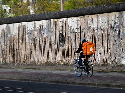 A Delivery Hero SE food delivery cyclist passes a preserved segment of the Berlin Wall on Bernauer Strasse in Berlin, Germany, on Monday, April 13, 2020. Germany saw its new coronavirus cases drop for the fifth consecutive day as the country considers whether to extend a nationwide lockdown beyond this week. 